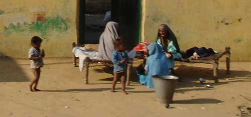 Family with small children sitting on beds in front of their house in the countryside.