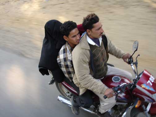 Two men and a muslim woman in black with face covered riding on one motor scooter.