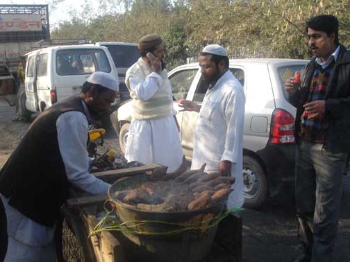 Man cooking potatos and his customers eating and talk on cell phone next to cars at railroad crossinig.