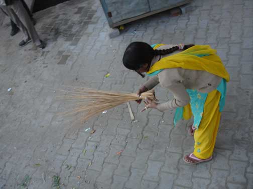 Woman sweeping street with broom with no handle.