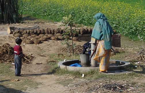 Woman pumping water with her little son watching.